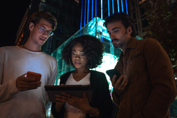 Three people looking at tablet with concentration while standing at the evening street