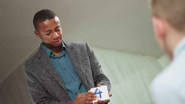 Positive African-American native speaker tutor shows cards with digits and letters pictures to little children at private tuition in room slow motion