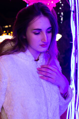 A girl in a coat and gloves stands under a Christmas tree decorated with lights. New Year 2022.