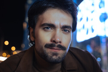 Man looking at the camera with pleasure smile while posing at the night street