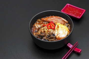 Ramen is a national, popular dish of traditional Korean cuisine. Asian soup with noodles, chicken breast, egg, mushrooms, broth, hot sauce and spices. Side view, copy space.