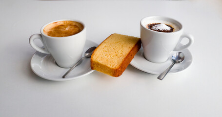 Two cups of coffee with milk, teaspoons, saccharin and a sponge cake seen from above on a white...