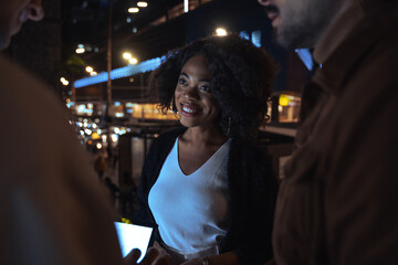 People standing together and smiling while working at the evening street with the tablet
