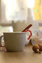 Cup of warm drink with candy cane and cinnamon stick, soft blanket and various Christmas decorations. Hygge at home. Selective focus.