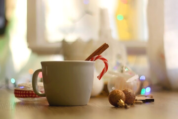 Cup of warm drink with candy cane and cinnamon stick, soft blanket and various Christmas decorations. Hygge at home. Selective focus.