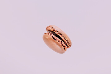 Chocolate macaron suspended in the air with purple background.