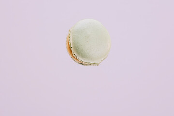 Pistachio colored macaron suspended in the air with purple background.