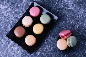 Different macarons of different flavors on a black plate.