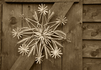 Christmas star (snowflake) made of straw on wooden wall of rural house in France. Sepia historic photo
