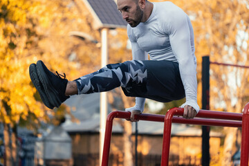 Good looking man doing abs on parallel bars outdoors in the hood