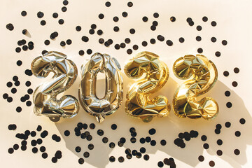 Balloons made of gold and silver foil in the form of numbers 2022 with confetti on a pink background . Celebrating Christmas, New Year and festive concept. Flat lay, top view.