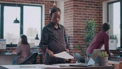 African american woman expecting child and working on business project with documents. Pregnant employee analyzing files to design and plan marketing strategy for development at office. - Powered by Adobe