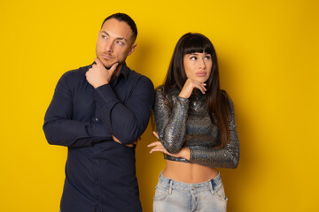 Disappointed young couple standing with arms folded over yellow background.