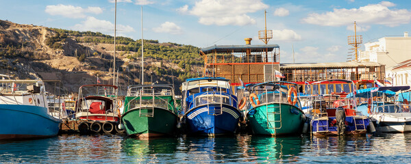 Fototapeta na wymiar Row of many small old multicolored vintage colorful bright fishing ships moored at fisherman village marina clear water bay on bright sunny day. Sea harbor with traditional retro vessels background