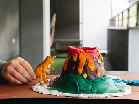 Faceless child playing with toy dinosaur after sculpting plasticine volcano