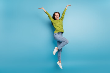 Photo of amazed funny lady jump raise arms wear green shirt jeans footwear isolated blue color...