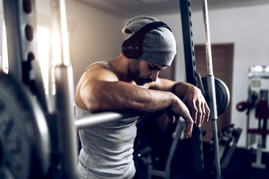 Shirtless man adjusting headphones before training with barbell