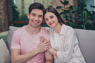 Portrait of attractive adorable cute cheerful spouses sitting on divan enjoying touching heart spending time at home indoors