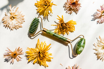 Green jade massager roller for the face on a white background next to dry buds of flowers. . High...