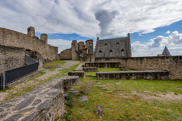 Lower courtyard of the upper part with dilapidated walls, roofs in the medieval castle of Bourscheid, cloudy day with a blue sky with abundant clouds in the background, Luxembourg