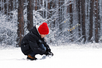 Fototapeta na wymiar A child in a red hat makes a snowman, plays with snow, the first snow, New Year's mood