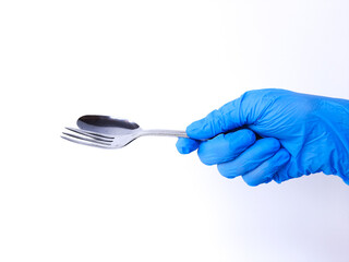A hand with blue latex glove holds metal spoon and fork. Isolated on a white background. Side view