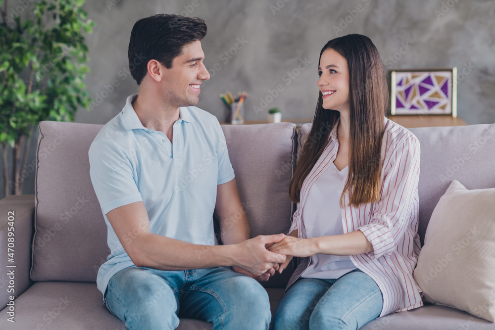 Sticker Portrait of attractive cheerful gentle romance couple holding hands sitting on divan spending time day at home indoors