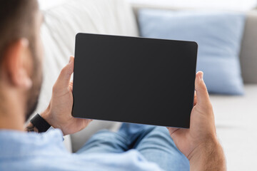 Millennial man on couch, relax and watch at tablet with empty screen, chatting at free time at home on self-isolation
