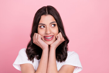 Photo of adorable happy young woman look empty space wear teeth braces isolated on pink color background
