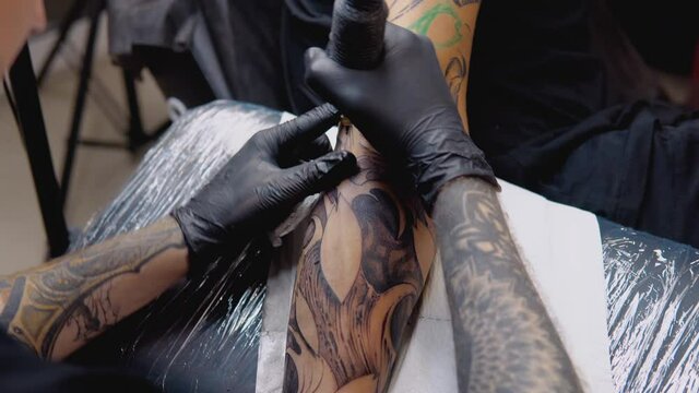 The process of tattooing with a tattoo machine with a woman's face on a man's hand in a tattoo parlor.
