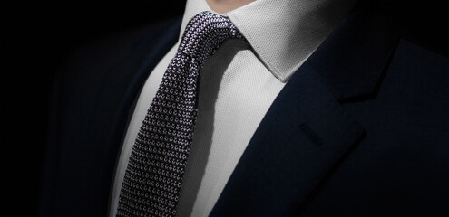 A dramatic close up shot of a man dressed in an expensive formal suit. The jacket is dark navy with...