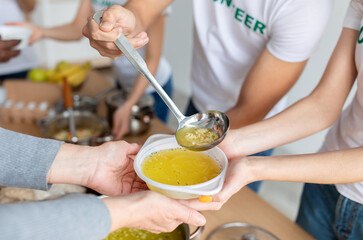 Volunteers serving hot soup for homeless in community charity donation center, group of young...