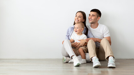 Beautiful Young Family With Little Baby Looking Aside While Relaxing On Floor