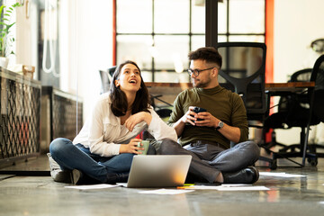 Fototapeta premium Colleagues sitting on the floor in office. Businesswoman and businessman working on the project.