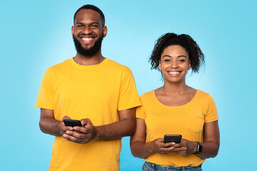 Affectionate young black couple using mobile phones, surfing internet, checking social media, sending sms messages