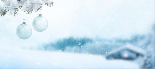 Fototapeta na wymiar Gläserne Weihnachtskugeln an einem Tannenzweig vor einem verschneiten unscharfen Hintergrund