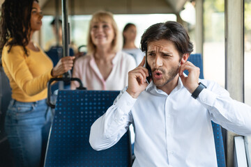 Confused guy talking on phone holding finger in ear - obrazy, fototapety, plakaty