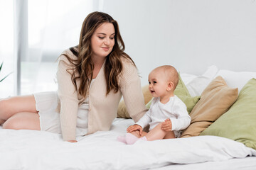 Happy plus size mother looking at smiling child on bed in bedroom.
