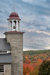 Colorful autumn sky, brilliant fall foliage, and granite bell tower of preserved textile mill building constructed in 1846 in historic village of Harrisville in New Hampshire. - obrazy, fototapety, plakaty