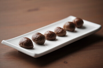Long white plate with 6 roasted chestnuts on a wooden table