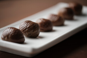 Long white plate with 6 roasted chestnuts on a wooden table