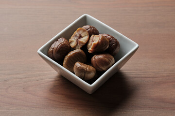 Square bowl with six roasted chestnuts on a wooden table