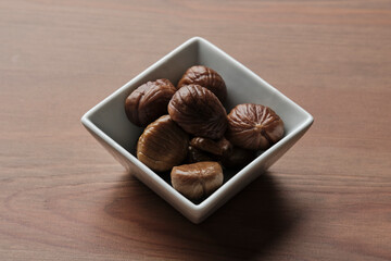 Square bowl with six roasted chestnuts on a wooden table
