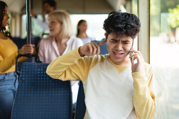 Young asian guy talking on phone plugging ear with finger