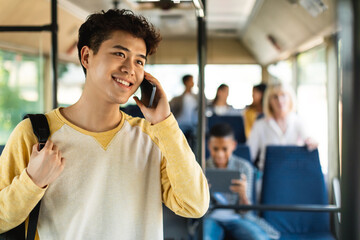 Smiling Asian guy taking bus, talking on cellphone © Prostock-studio