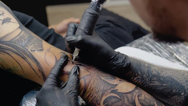 A tattoo artist with a tattooed arm makes a full arm tattoo to his client. Artistic permanent image on the human body