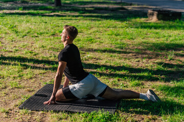 Healthy young man doing outdoors warmup stretching exercises on a fitness mat