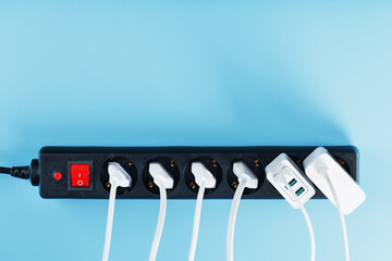 Electric mains filter with inserted white plugs of electrical appliances on a blue background.