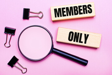 On a pink background, a magnifier, black paper clips and wooden blocks with the text MEMBERS ONLY....