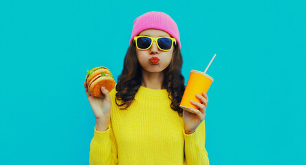 Portrait of stylish young woman with burger and cup of juice fast food on blue colorful background